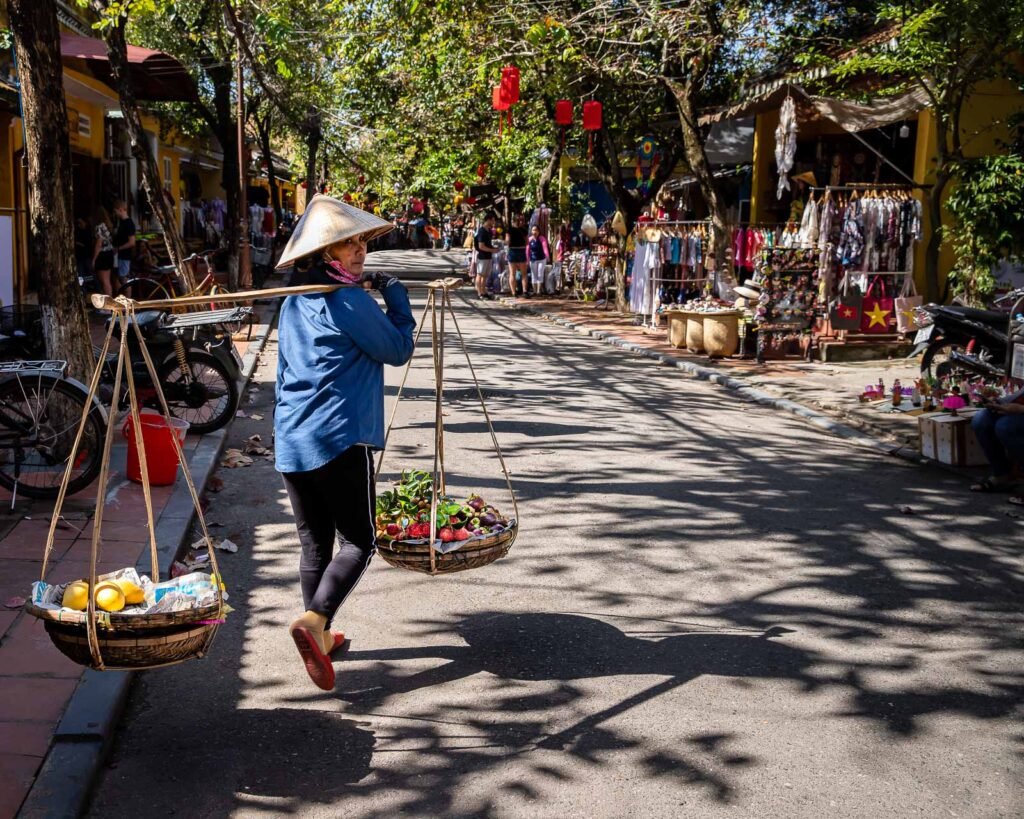 vietnamese woman with traditional hat walking with baskets of food in the street in hoi an